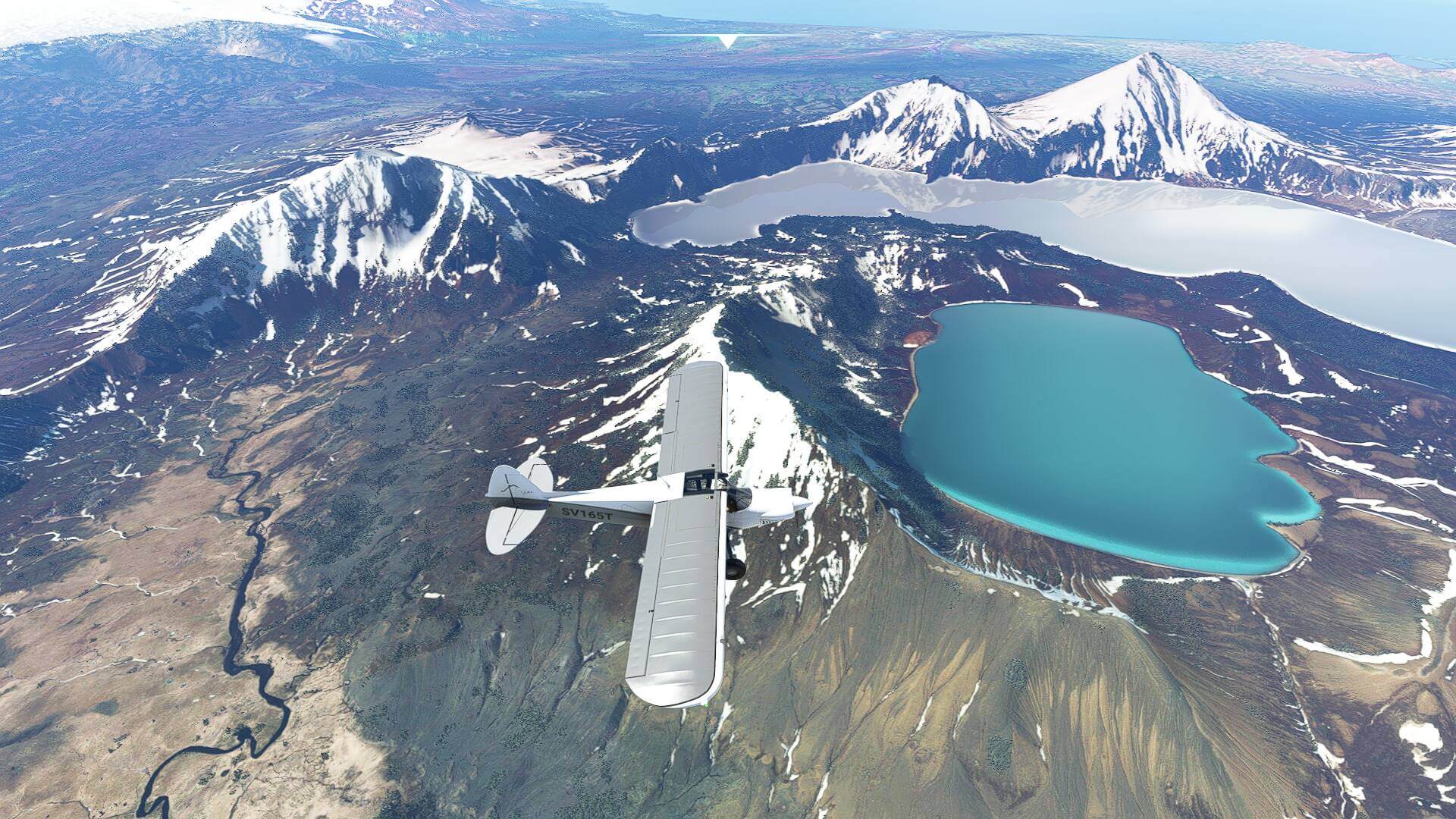 Plane flying over a blue lake in the snowy mountains